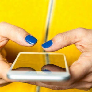 woman wearing yellow sweater with blue nails holding iphone