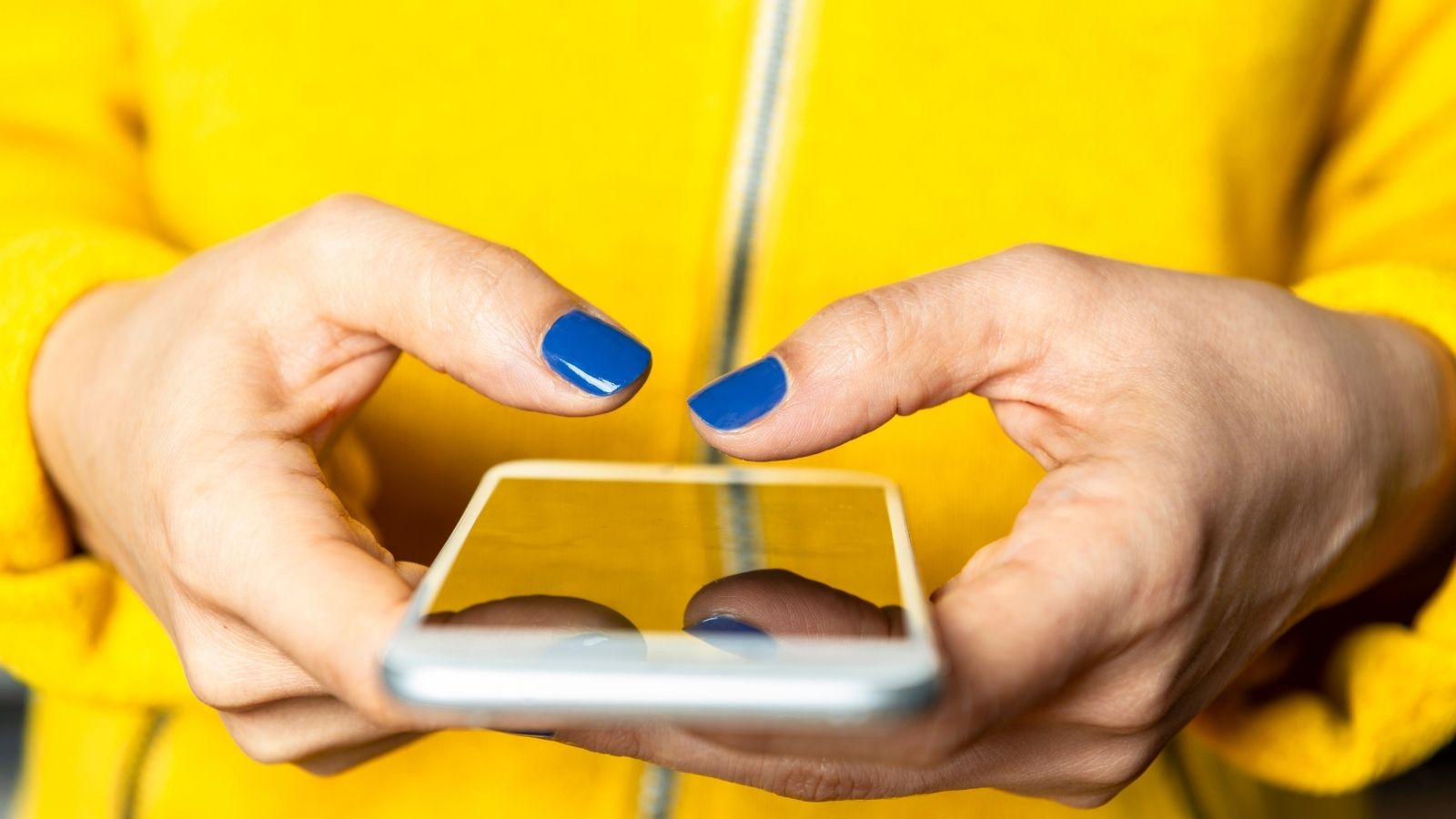woman wearing yellow sweater with blue nails holding iphone