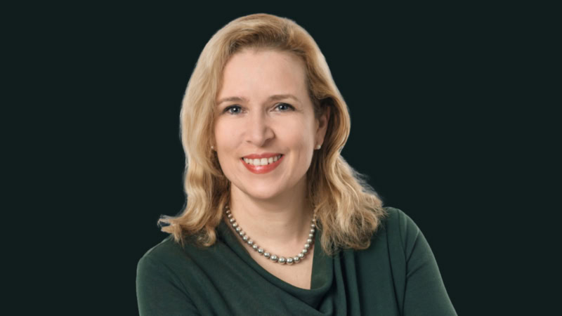 Mature blond woman in a green dress smiles at camera