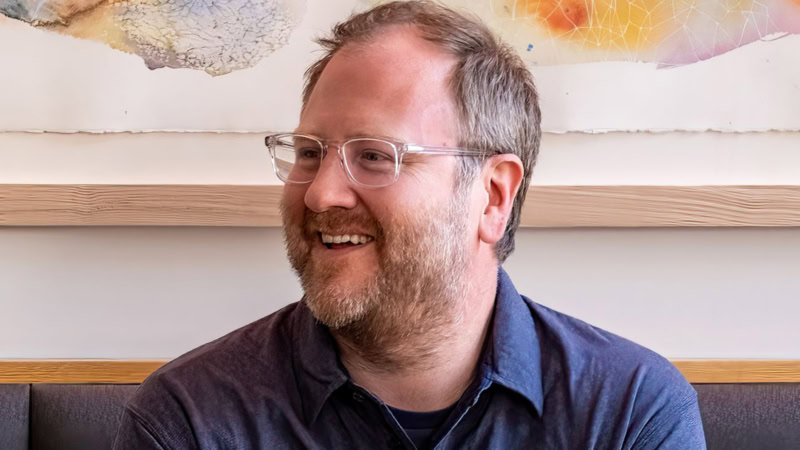 Dan Petroski wearing a blue shirt and smiling at something to the left of camera