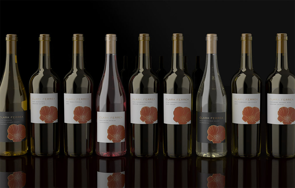 A row of nine Clark Ferrea wine bottles with labels, seven featuring a red poppy design on a beige label and two with clear labels, on a reflective surface against a dark background.