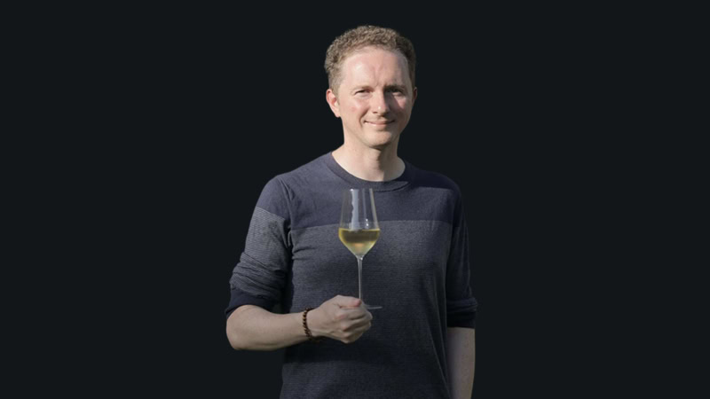 A young man in a blue shirt holds a glass of wine.
