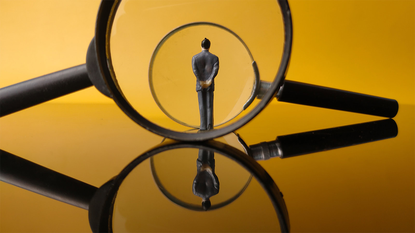 Miniature people center of a magnifying glass with reflection on a yellow background.