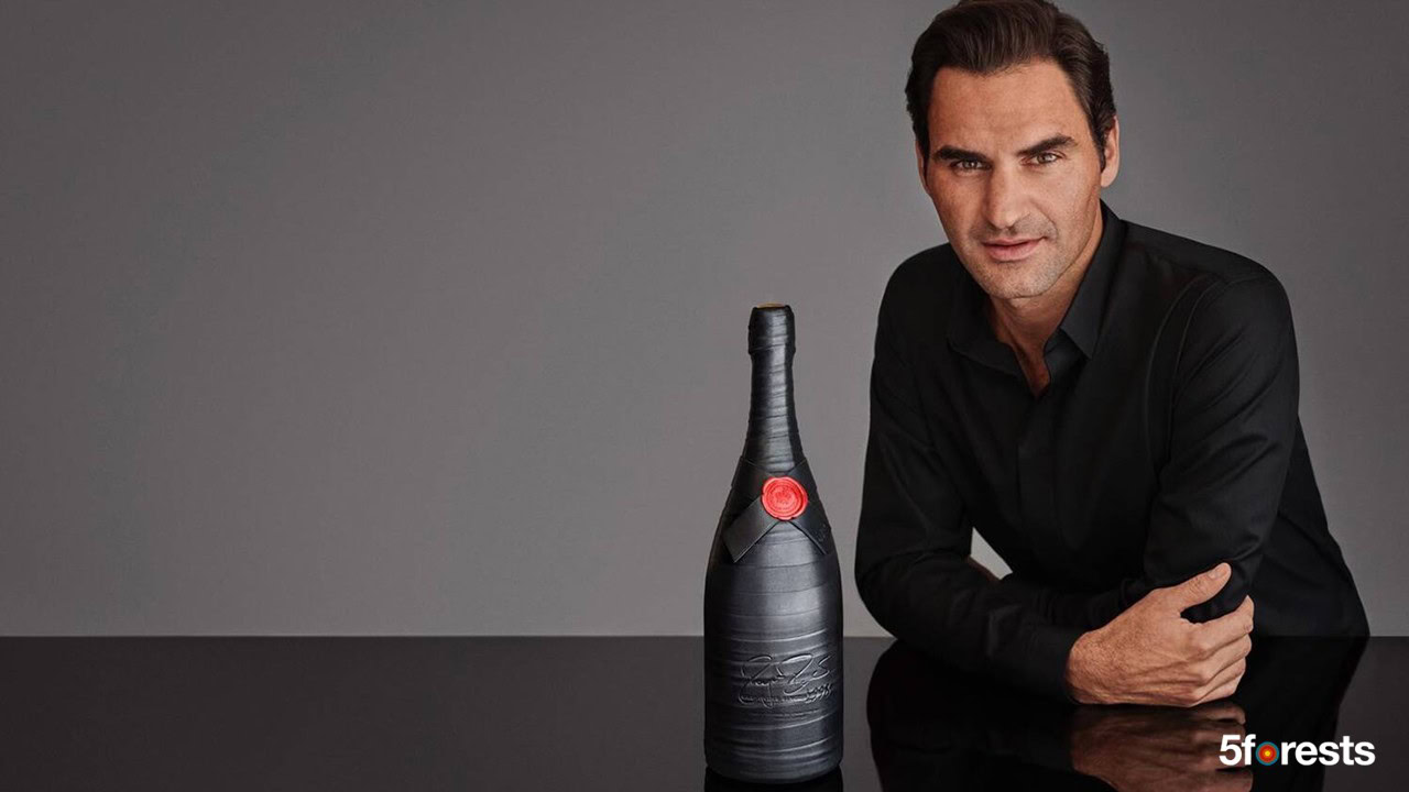 A man in a black shirt sits at a reflective black table next to a dark bottle with a red seal. 