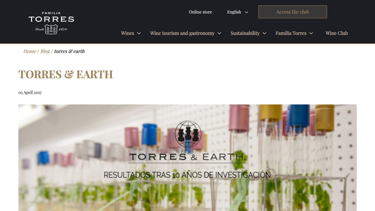 A laboratory scene with glass test tubes containing green plants, featured on the Familia Torres website under the "TORRES & EARTH" research blog post header.