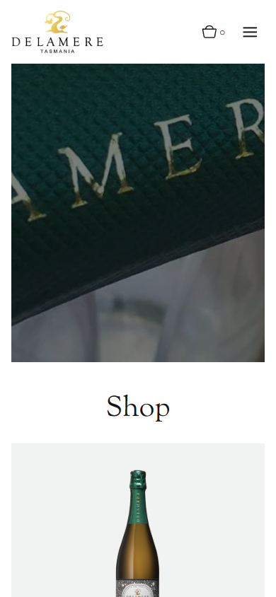 The Delamere shop on a phone, with an embossed green foil close-up above the heading "Shop" and the first sparkling bottle.