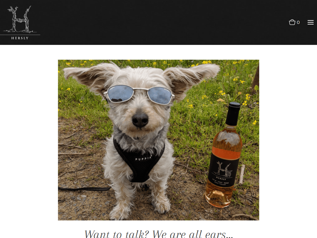 The Hersly Wines contact page on desktop: a small dog wearing sunglasses sitting beside a Hersly bottle, under the line "Want to talk? We are all ears..."