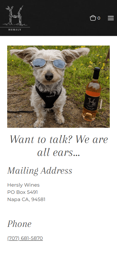 The Hersly Wines contact page on a phone, with the dog-and-bottle photograph, the line "Want to talk? We are all ears...", and the mailing address and phone number.