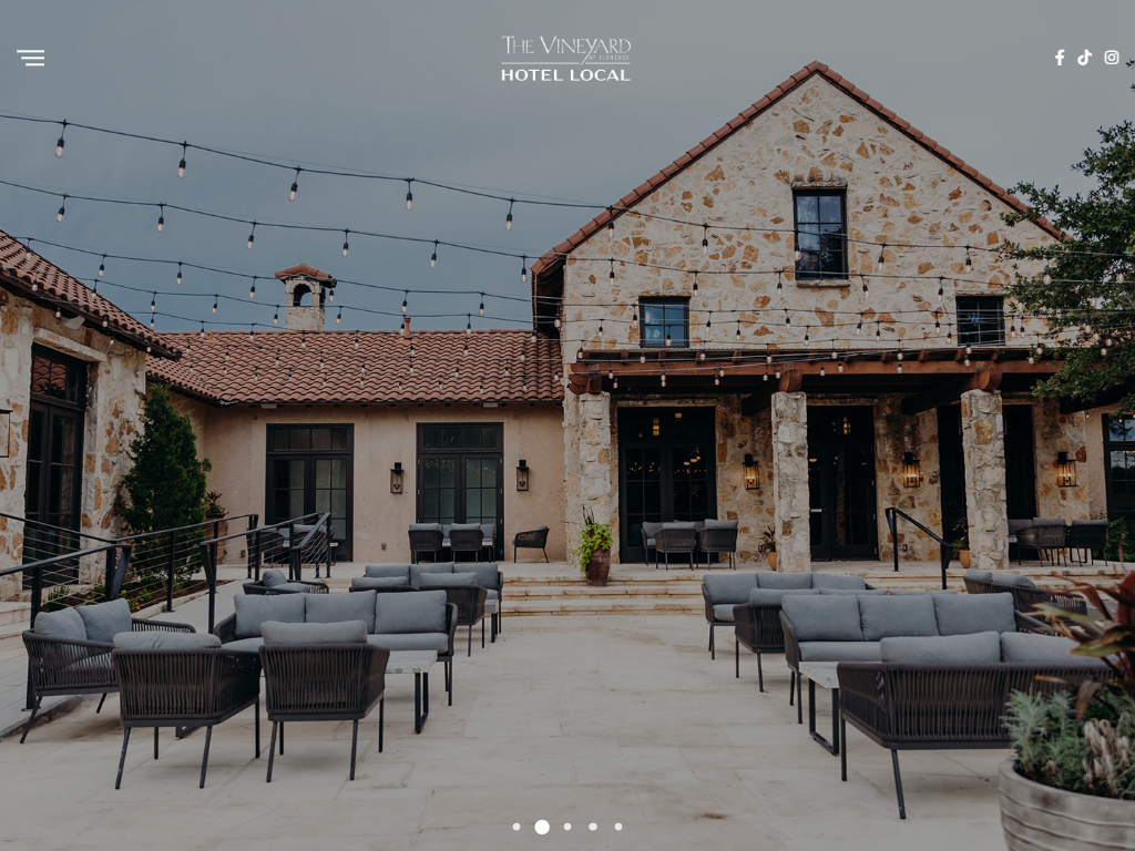 The Vineyard at Florence tasting room page in a desktop browser, with the stone building at dusk and its furnished terrace strung with lights.